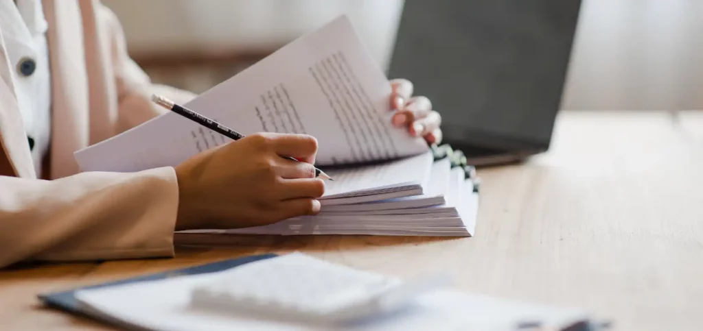 Person reviewing documents and taking notes at desk with laptop