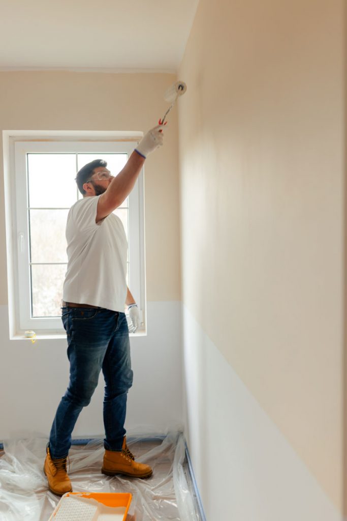 Worker repainting interior walls in an older residential property where lead-based paint may still be present beneath newer paint layers in pre-1978 homes.