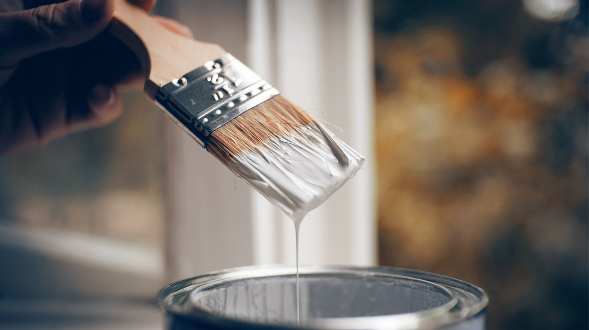 Close-up of paint brush applying white paint during residential repainting project in an older home where lead-based paint hazards may exist before 1978 ban.