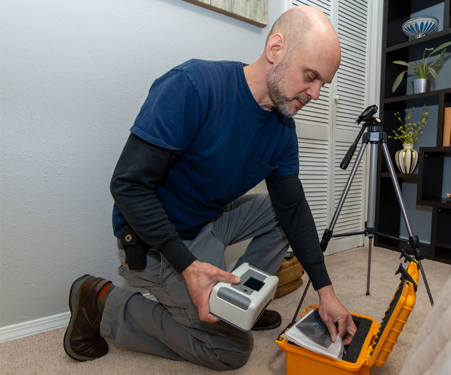 Technician setting up a professional radon test monitor inside a home during a residential radon inspection