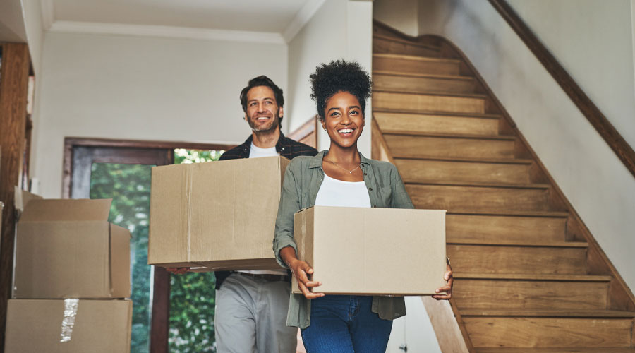 Homebuyers carrying moving boxes into a newly purchased house, representing residential air quality testing during a real estate transaction.