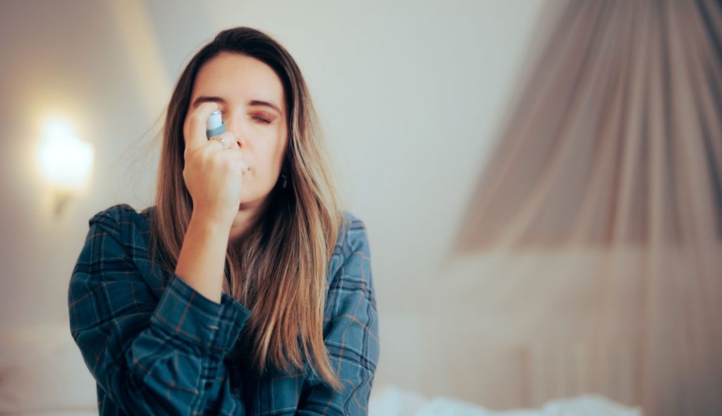 Woman using an inhaler while experiencing respiratory symptoms associated with indoor mold exposure
