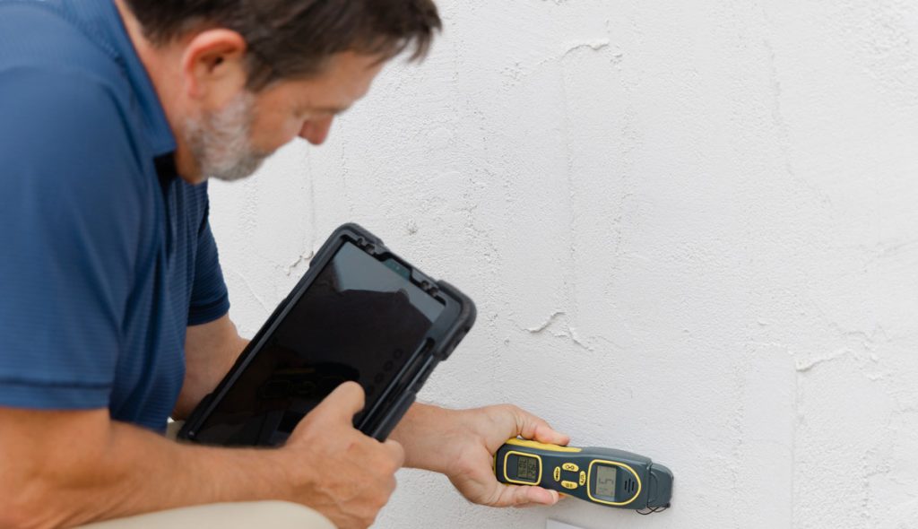 Mold inspector using a moisture meter to check a basement wall for hidden moisture problems