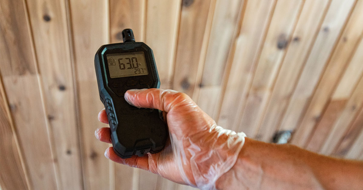 Handheld indoor air quality monitor testing VOC levels near wood building materials.